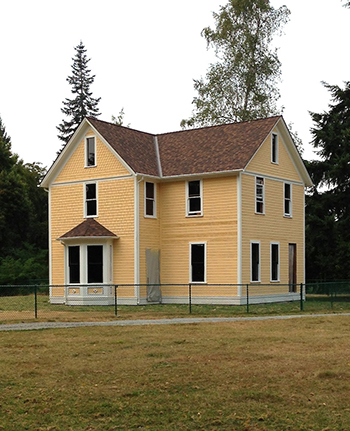The Reard Freed House -a yellow 19th century two-story farmhouse with white trim. Some windows and the doors are missing.